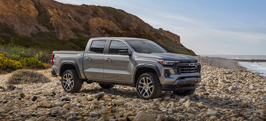 2025 Chevrolet Colorado parked on a rocky beach with coastal cliffs in the background.