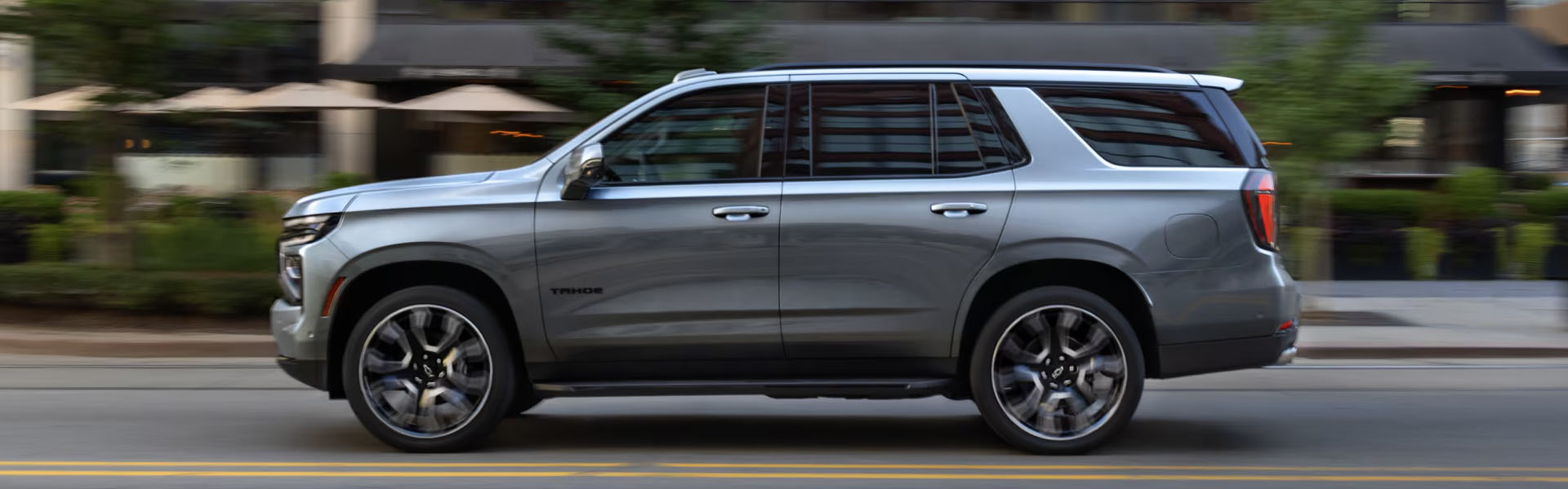 2025 Chevrolet Tahoe SUV driving through an urban street, showcasing its large body design, modern styling, and premium alloy wheels.